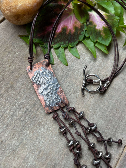 Copper & Silver Pendant with Leather Fringe on wood with leaves