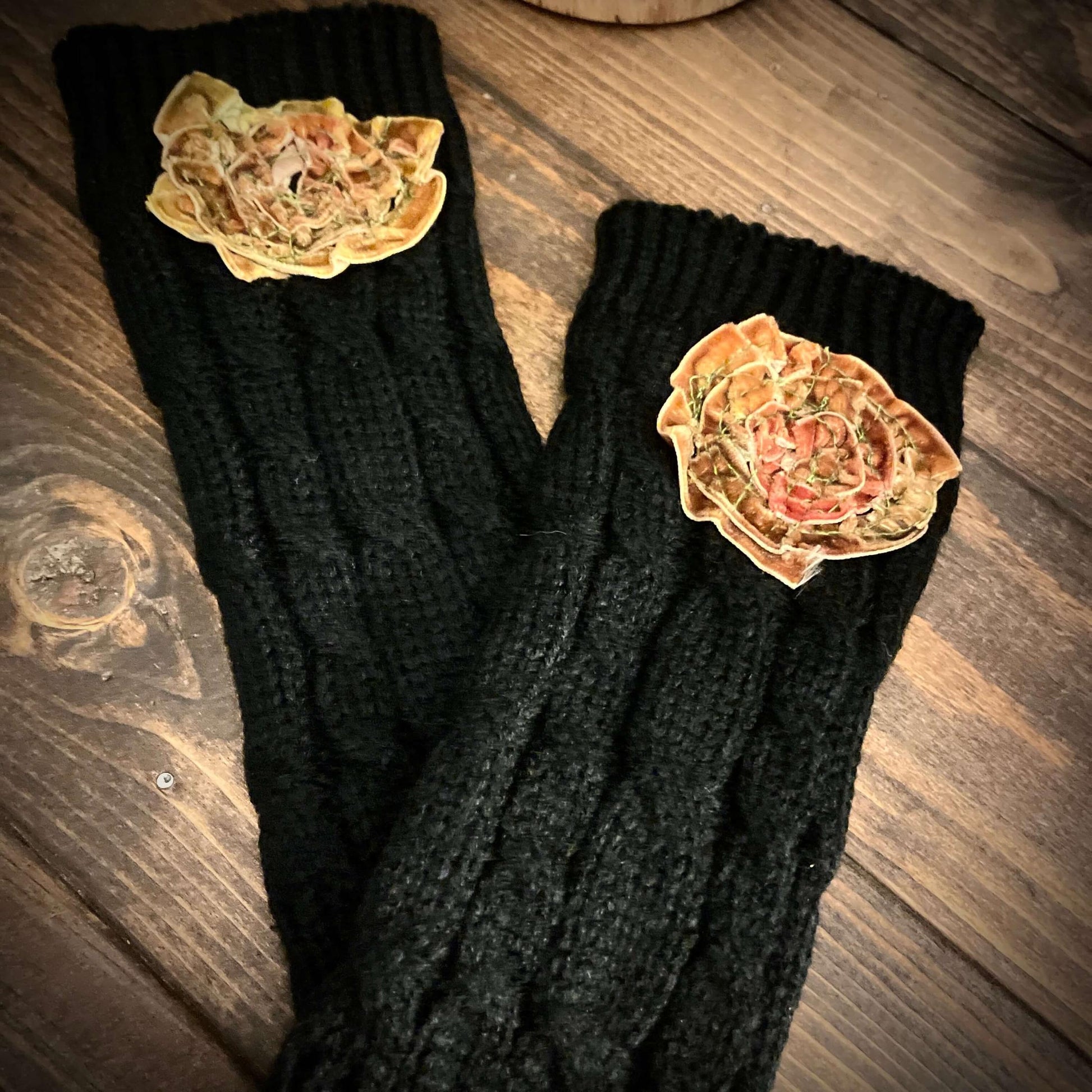 Black knitted gloves with decorative flowers on a wooden surface