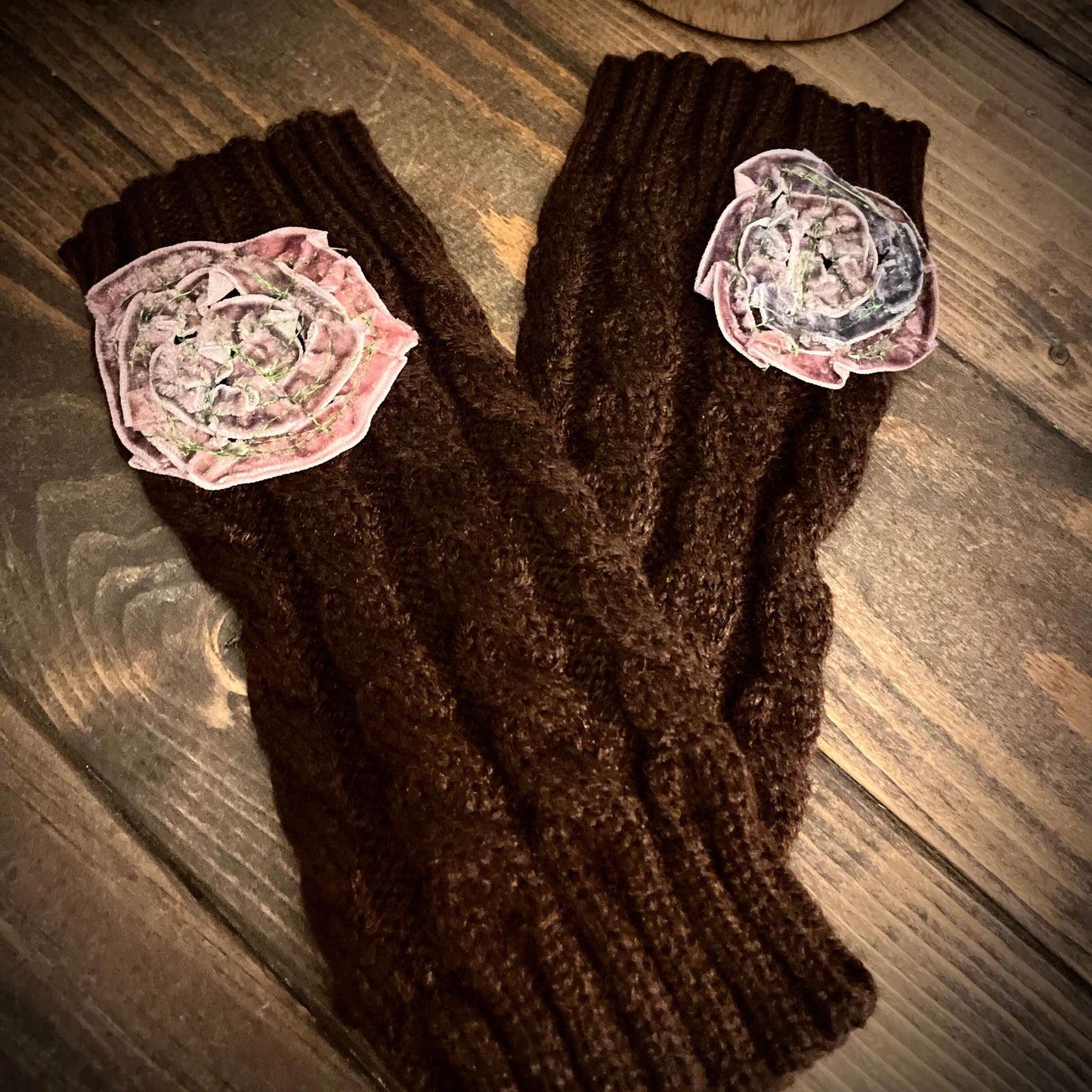 Brown knitted gloves with floral patches on a wooden surface
