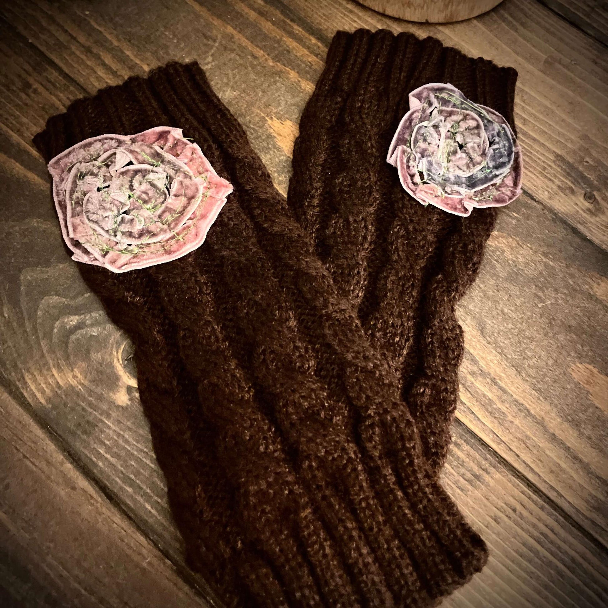 Brown knitted gloves with floral patches on a wooden surface